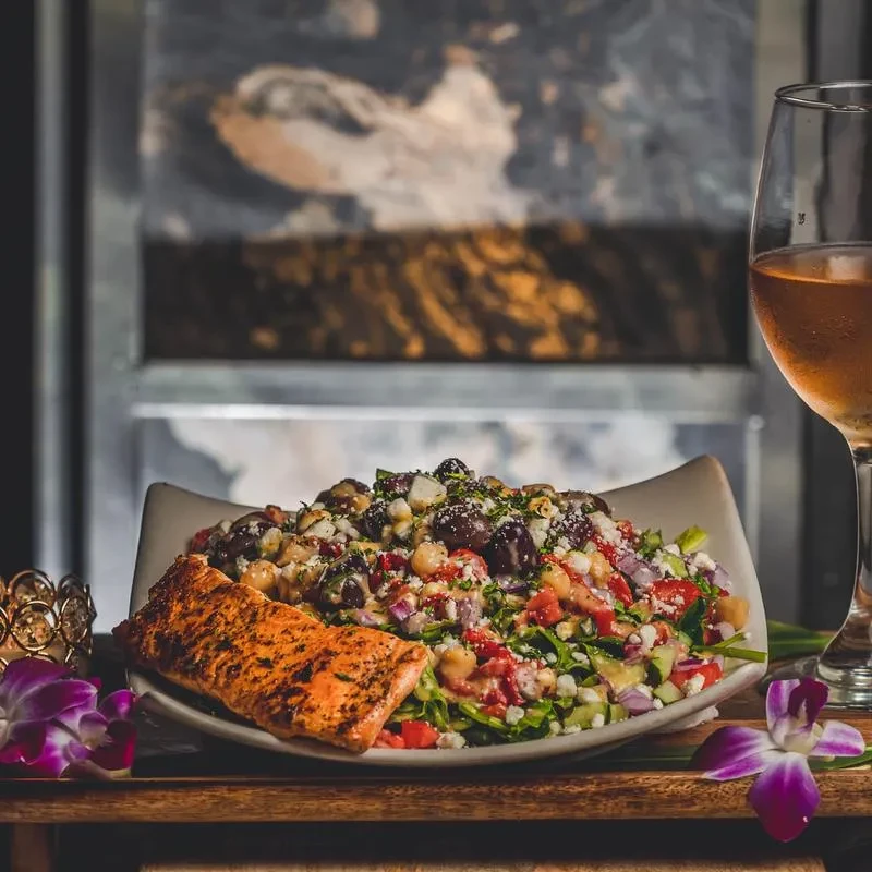 Beautifully plated vibrant salad, grilled salmon, wine, and purple orchids.