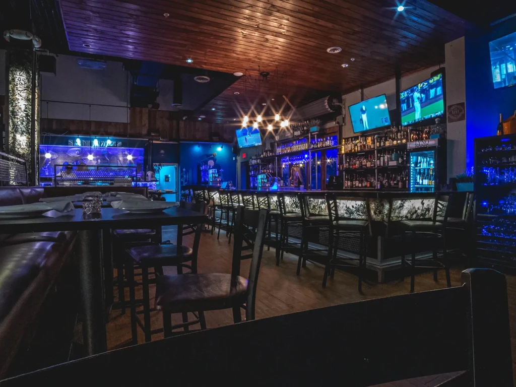Dimly lit modern bar restaurant with blue LEDs and wooden ceiling.