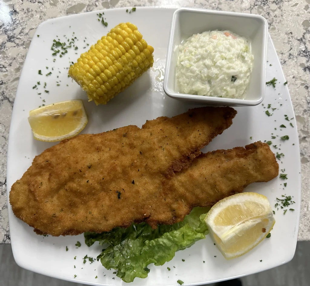 Fried fish, corn, coleslaw, and lemon on a white plate.
