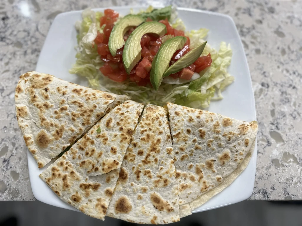 White plate with golden quesadilla triangles and avocado side salad.