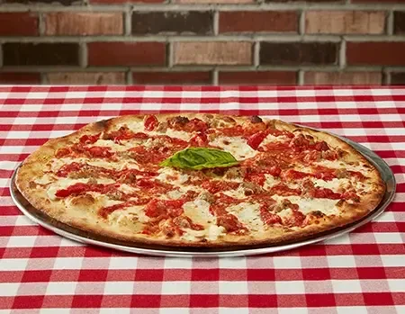 Classic pizza with sausage, cheese, sauce, and a fresh basil leaf.
