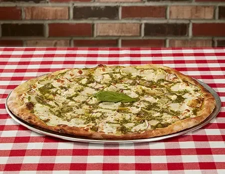 Oval pizza with white sauce, green pesto, and basil on checkered tablecloth.