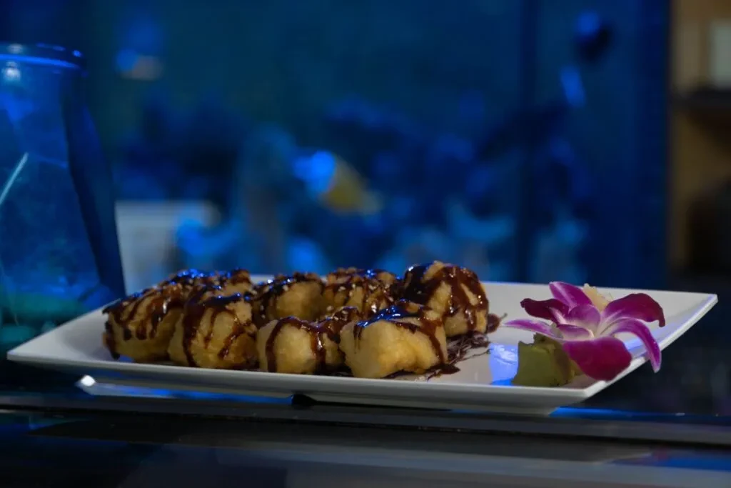 Golden-brown fried food with dark sauce, sesame seeds, orchid, green paste.