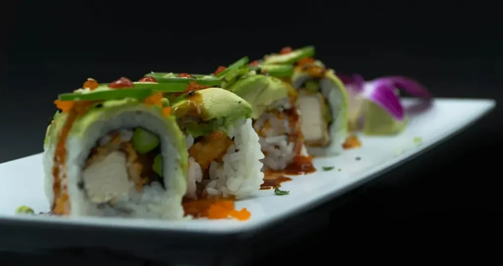 Platter of avocado and tobiko sushi rolls with sauce and orchid garnish.