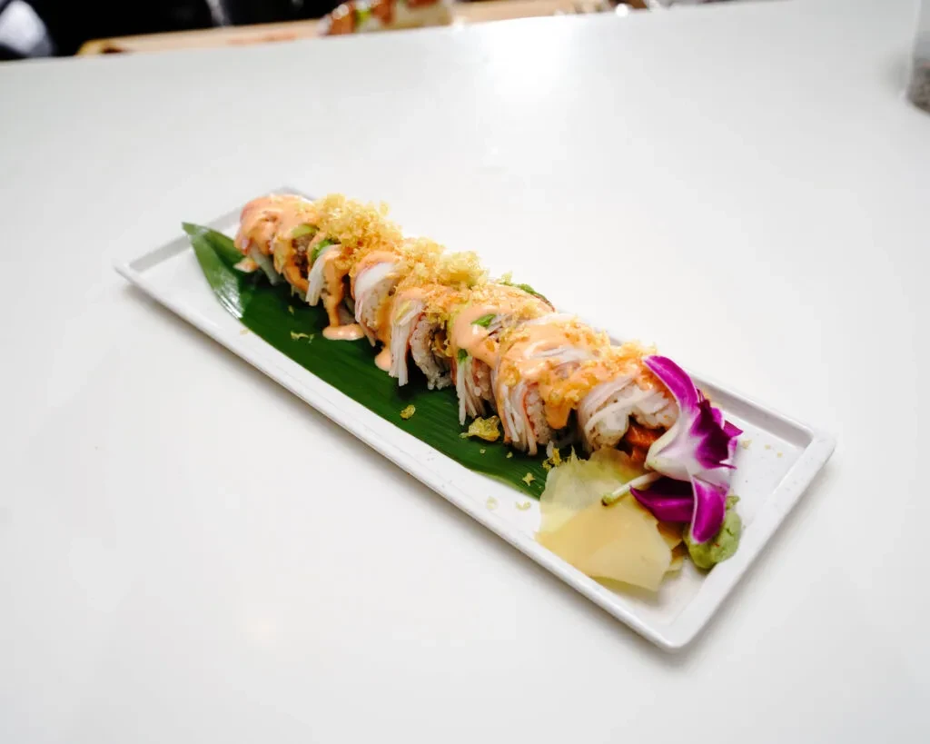 Sushi rolls with creamy sauce, fried flakes, wasabi, ginger, and orchid.