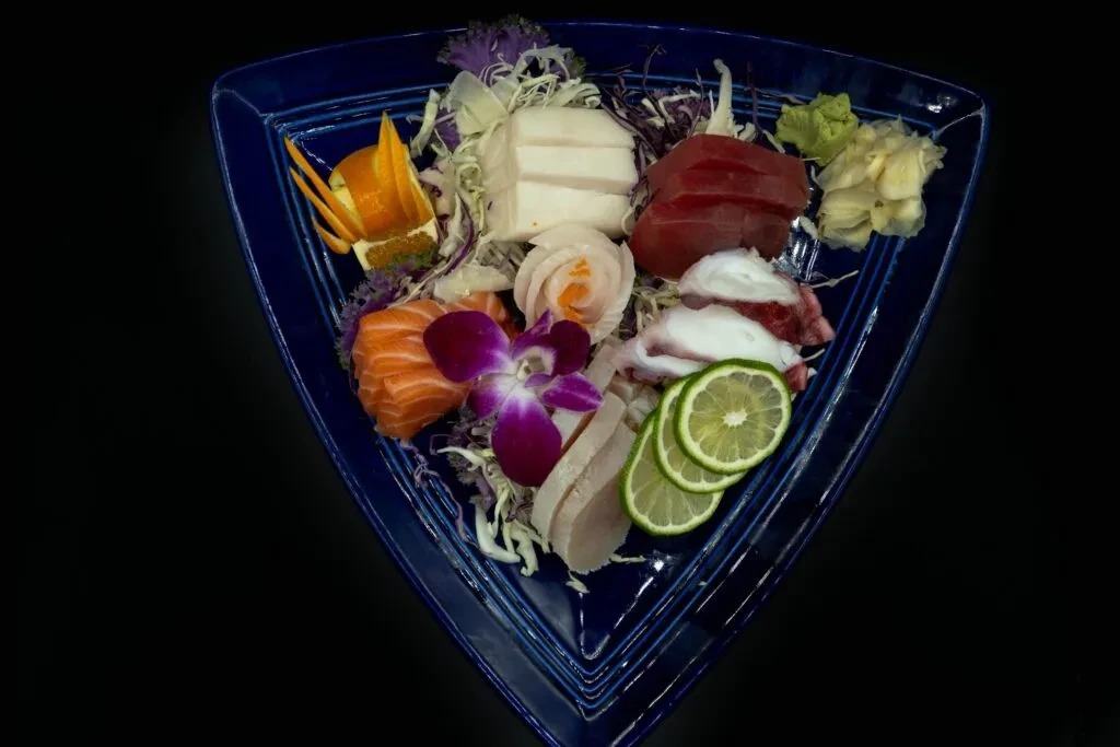 Artistic sashimi platter with salmon, tuna, octopus, and purple orchid.