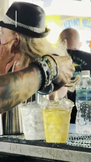 Tattooed bartender in fedora pours drinks from a cocktail shaker.