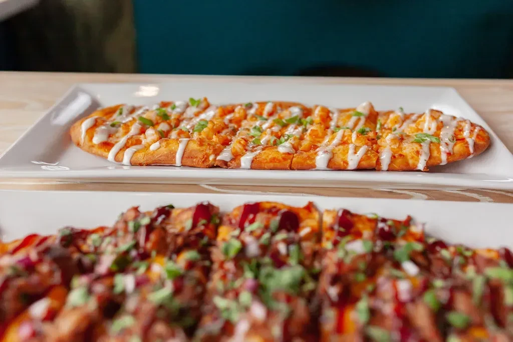 Two rectangular flatbreads; buffalo chicken in focus, another blurred below.