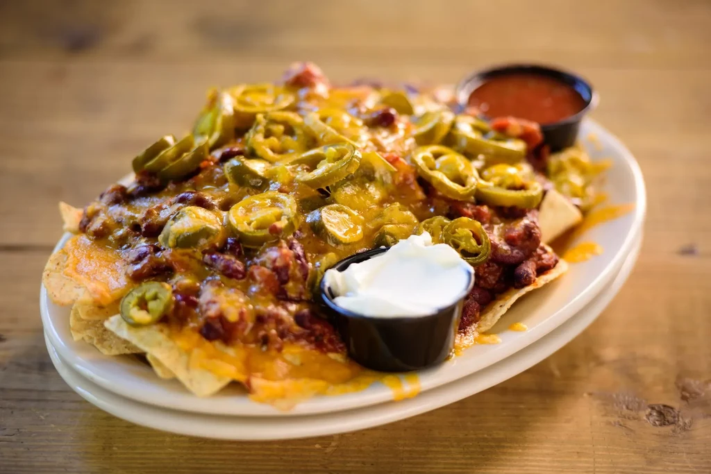 Nachos with melted cheese, chili, jalapeños, sour cream, and salsa on wood.
