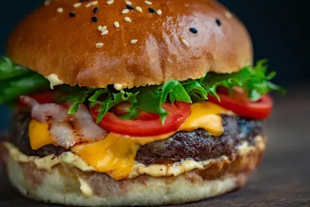 Gourmet burger with sesame bun, lettuce, tomato, melted cheese, bacon, patty.