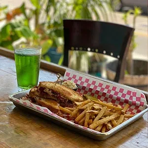 A sandwich, french fries, and green drink on a wooden table.
