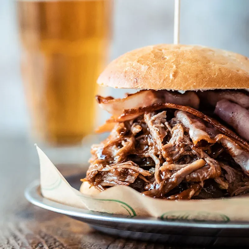 Hearty pulled pork and bacon sandwich on a rustic metal plate.