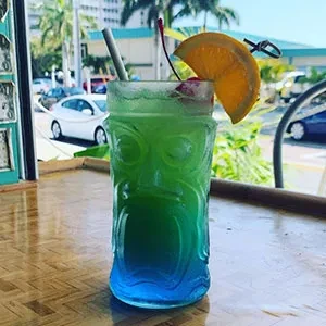 Green-blue gradient cocktail in tiki glass, cherry, orange garnish.