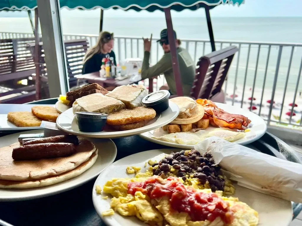 Abundant breakfast spread on a patio overlooking beach and ocean.