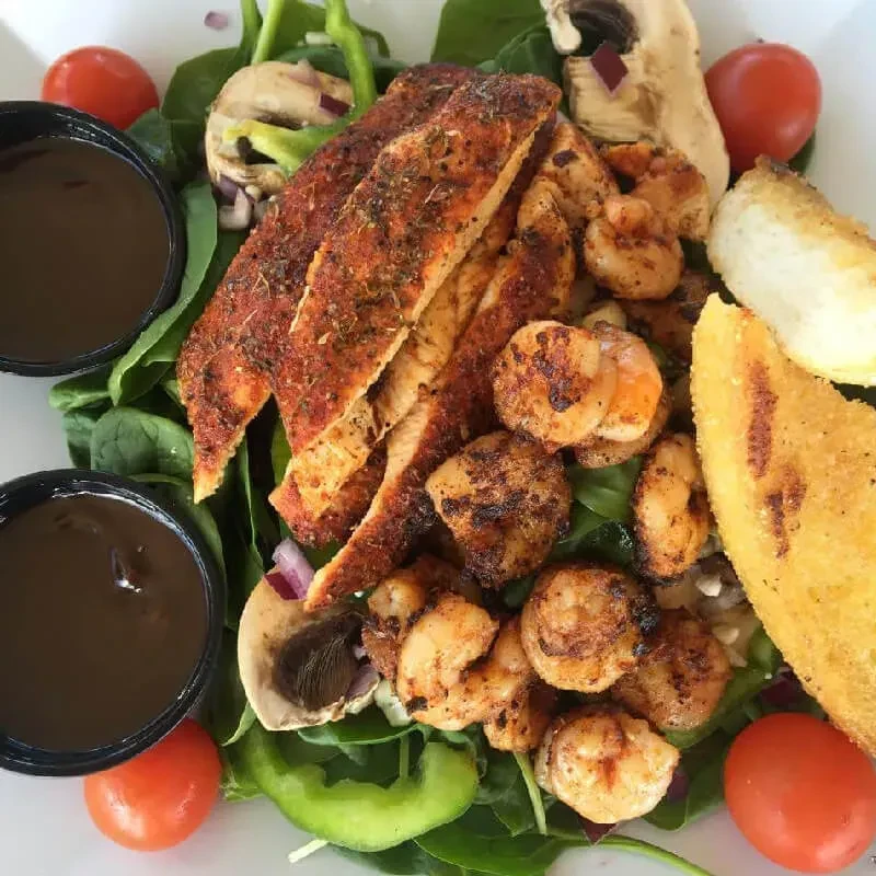Grilled chicken, shrimp, and vegetable salad with sauce and bread.