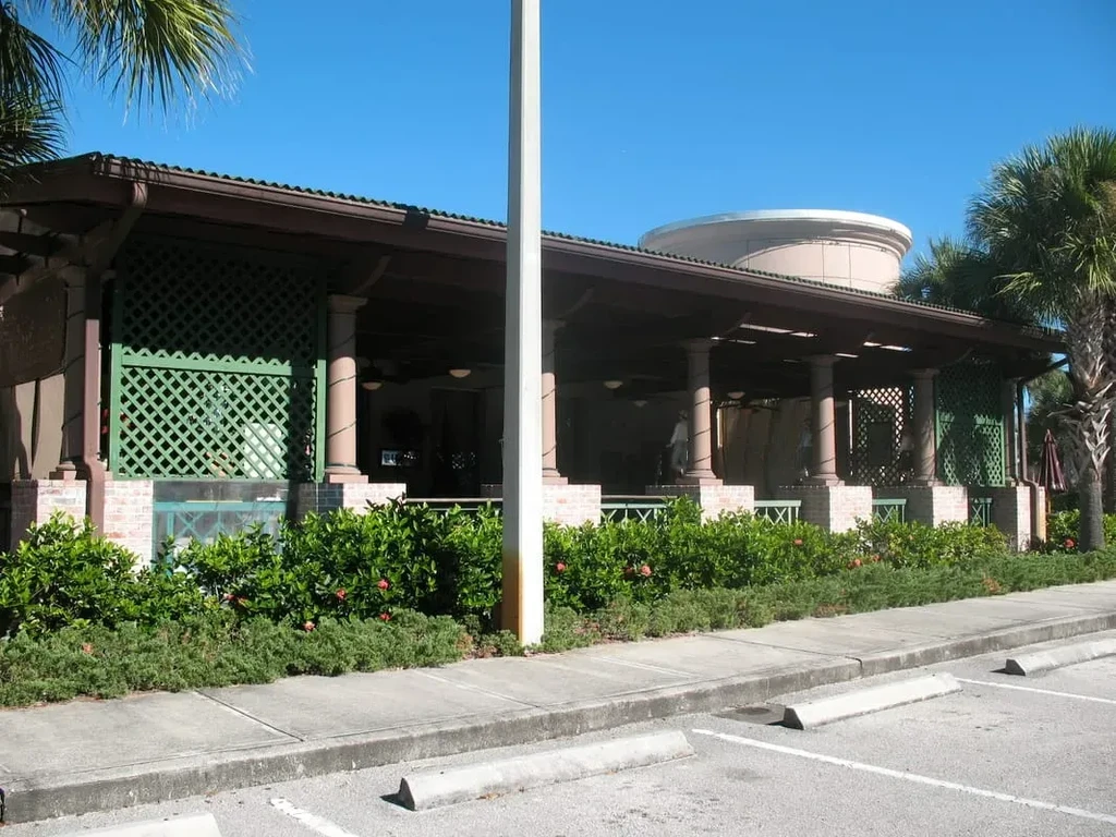 Sunny building exterior with covered patio, green lattice, and palm tree.