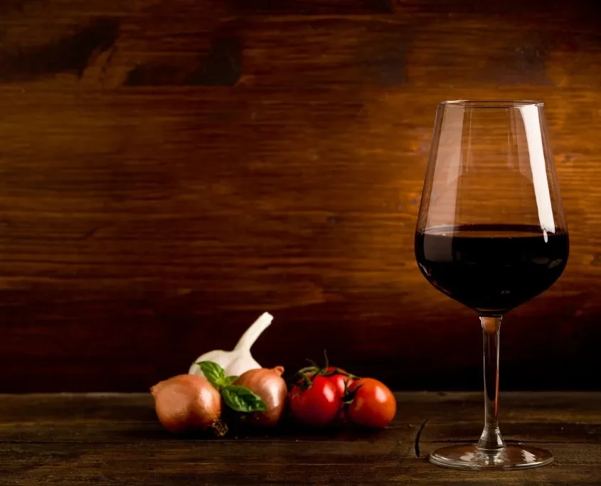 Red wine glass, garlic, shallots, tomatoes, and basil on dark wood.