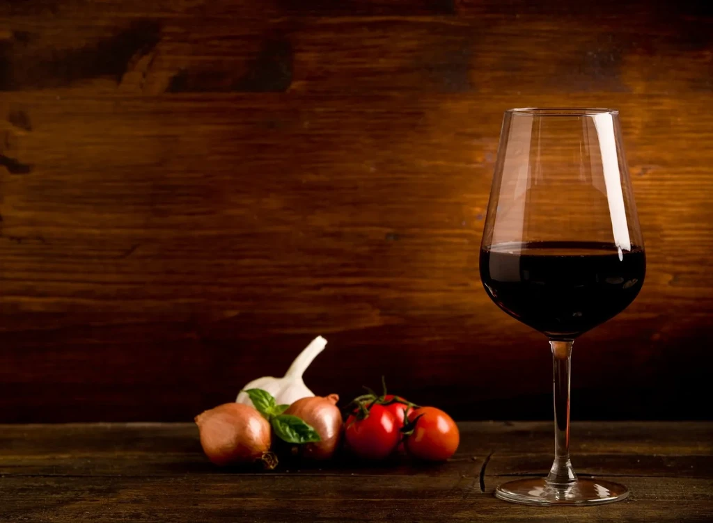 Still life: red wine, garlic, onions, basil, tomatoes on dark wood.