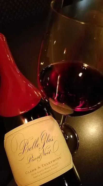 Belle Glos Pinot Noir bottle and wine glass in dim, warm light.