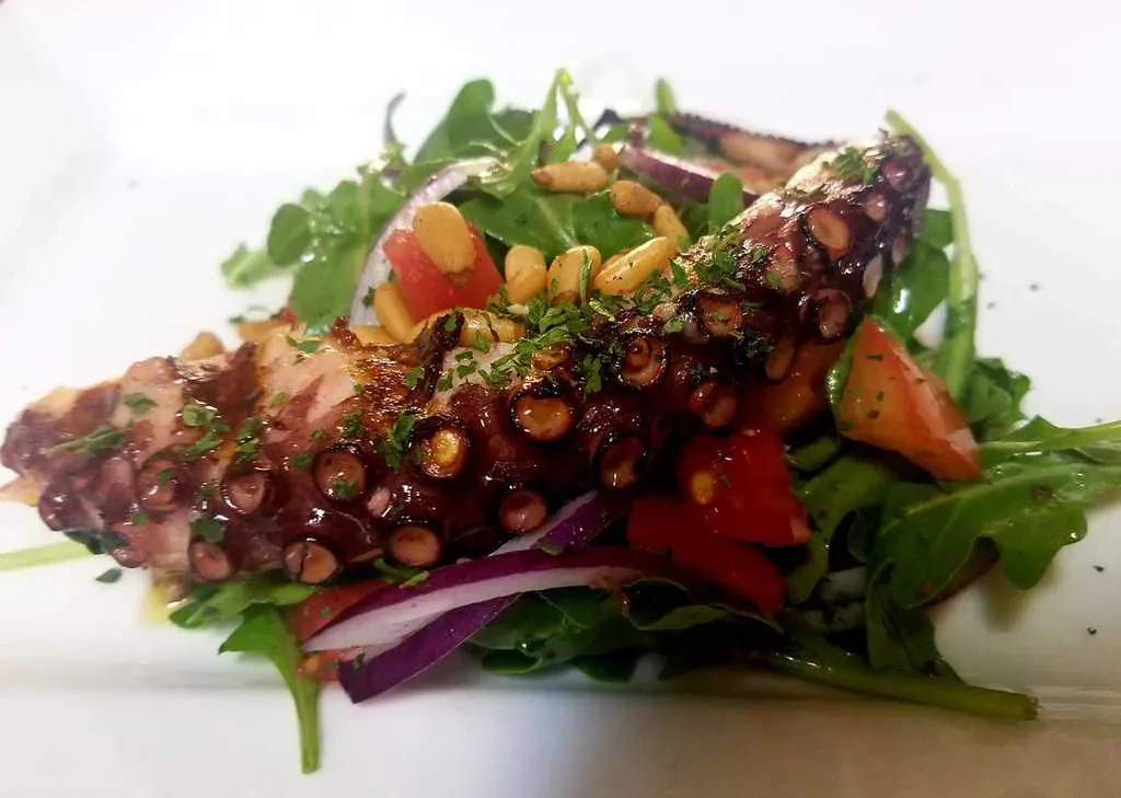 Charred grilled octopus with greens, tomatoes, herbs, and pine nuts.