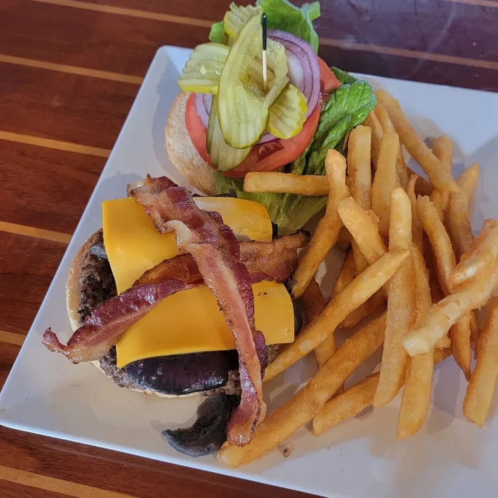 Open-faced bacon cheeseburger with lettuce, tomato, pickles, and fries.