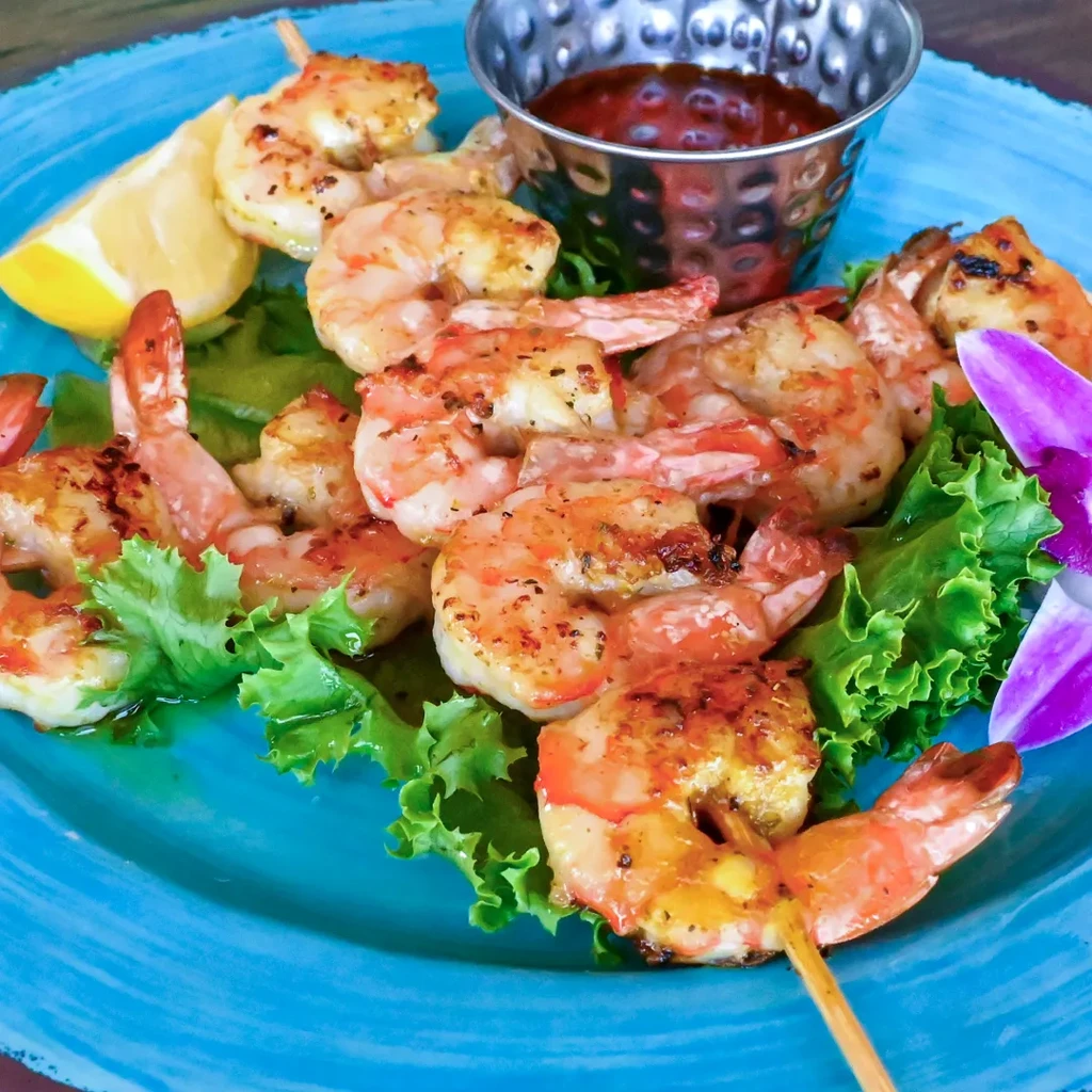 Blue plate with grilled shrimp skewers, lettuce, lemon, sauce, and orchid.