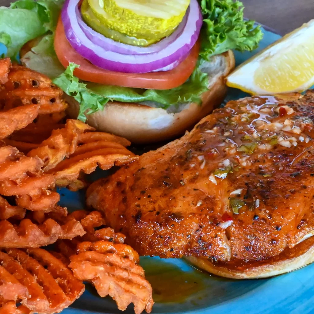 Seared fish, waffle fries, and burger with pickle on a teal plate.