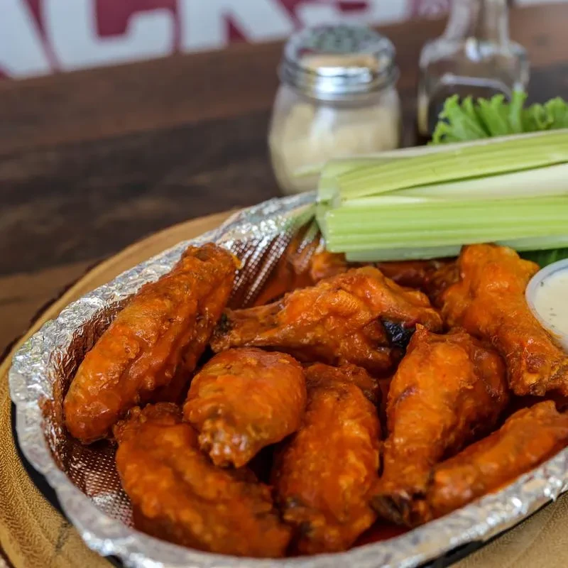 Glistening buffalo wings, dip, and celery in a foil-lined basket.