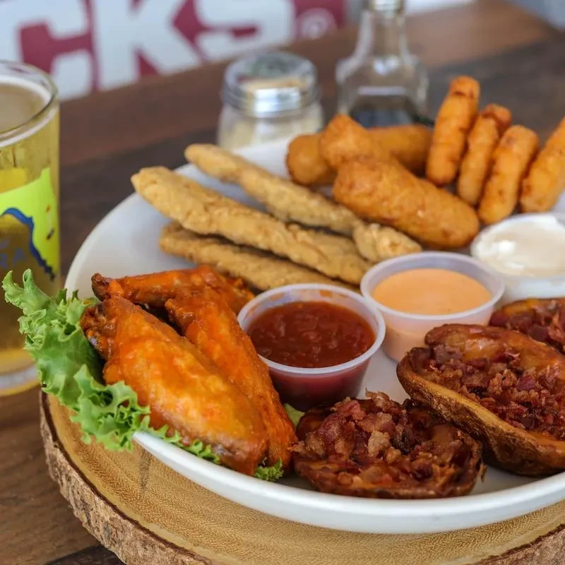 Appetizer platter with buffalo wings, potato skins, fried foods, sauces, and beer.