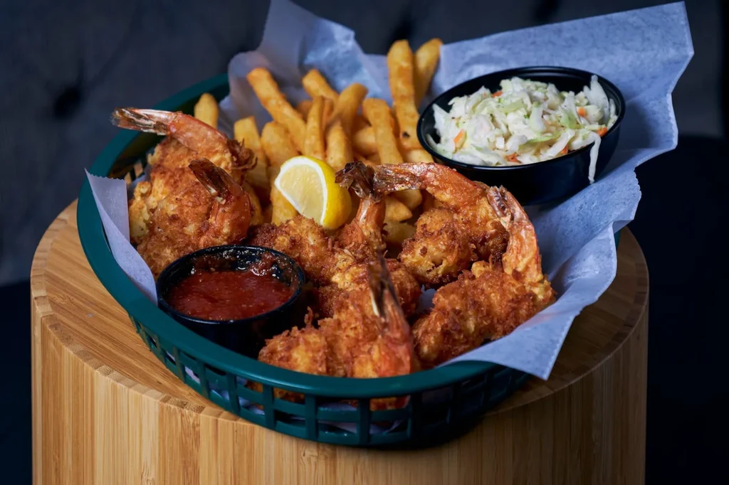 Fried shrimp, fries, coleslaw, and dipping sauce in a green basket.