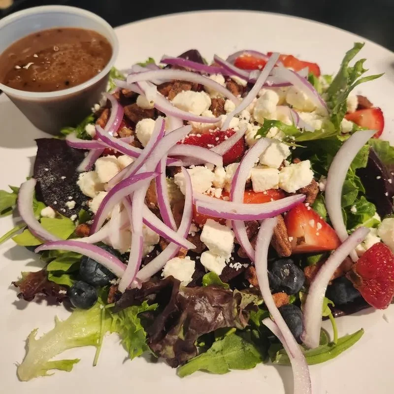 Colorful mixed green salad with strawberries, blueberries, feta, pecans, and dressing.