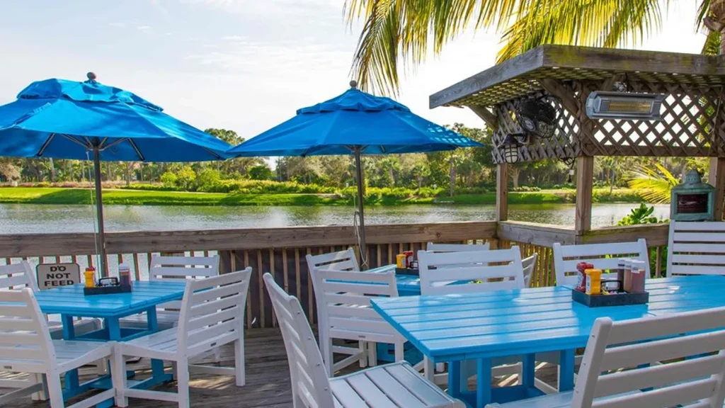 Empty tropical waterfront deck with blue picnic tables and umbrellas.
