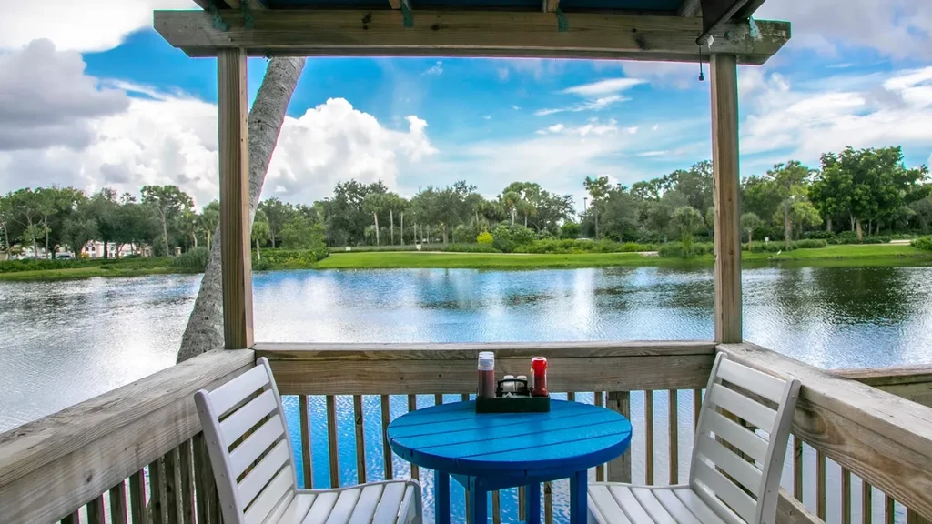 Waterfront deck with blue table, white chairs, overlooking a lake.