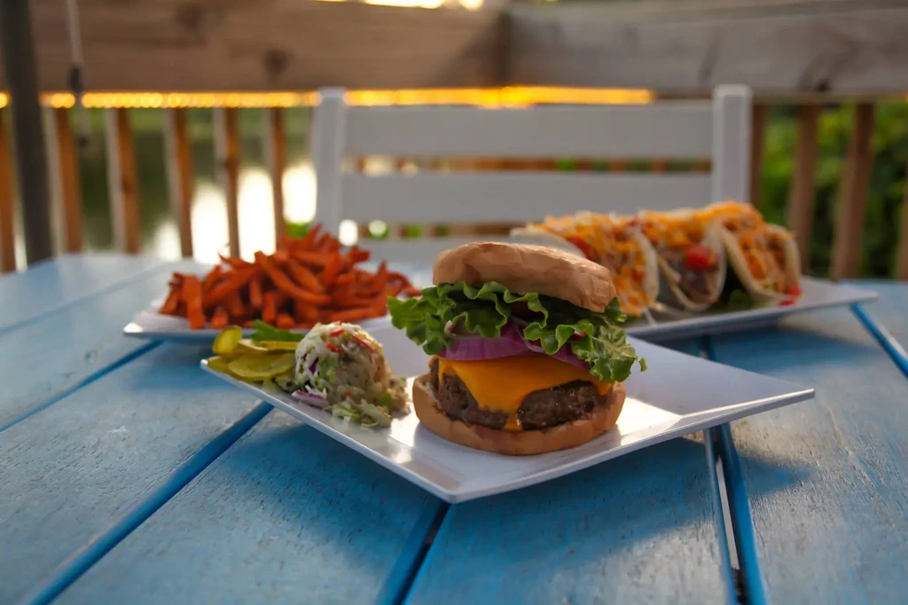 Cheeseburger, sweet potato fries, and tacos on blue wooden table.