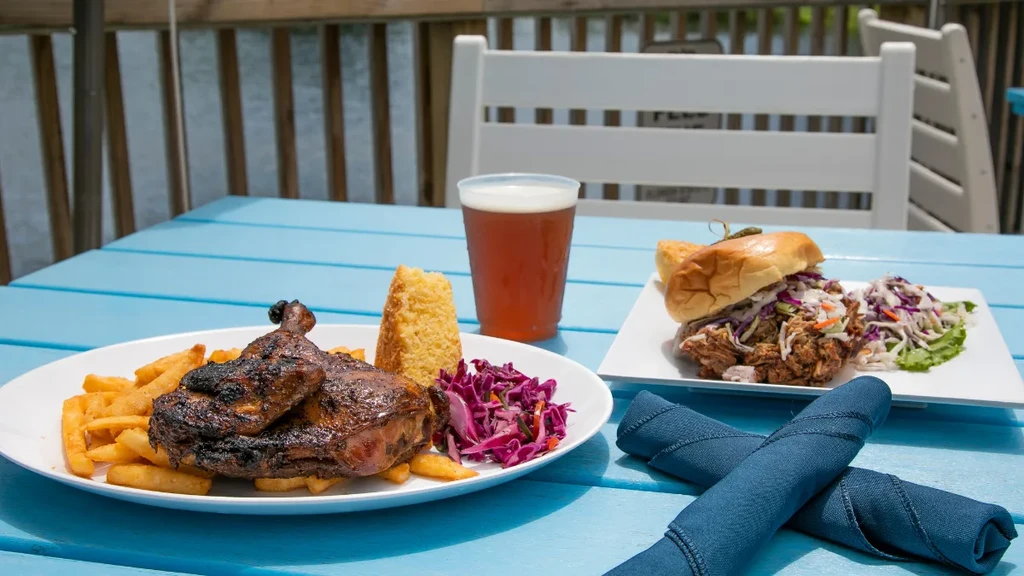Grilled poultry, pulled sandwich, fries, and drink on blue patio table.