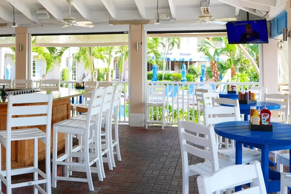 Bright semi-outdoor resort bar area with blue tables and palm trees.