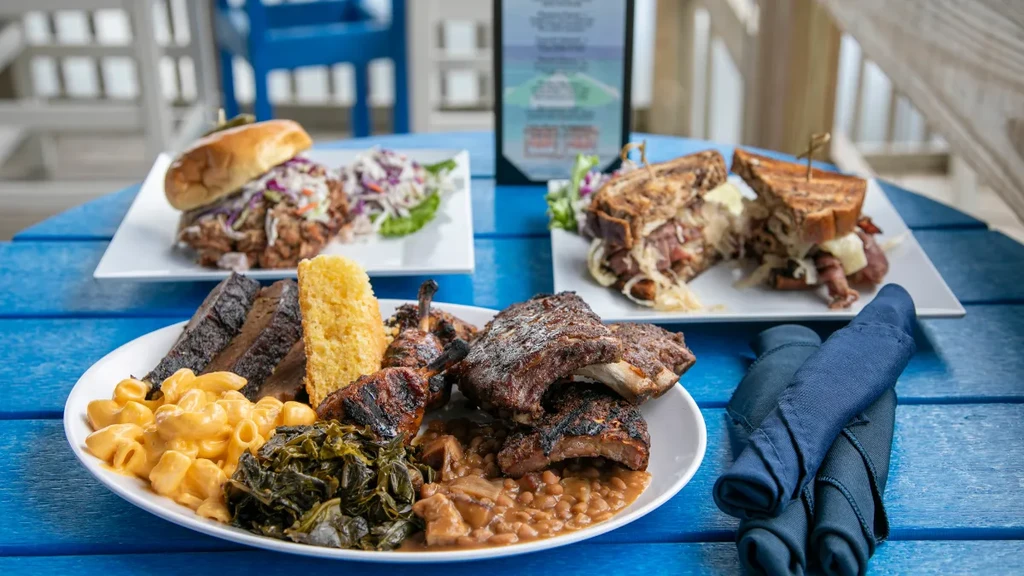 Blue patio table with barbecue ribs, pulled pork, and sandwiches.