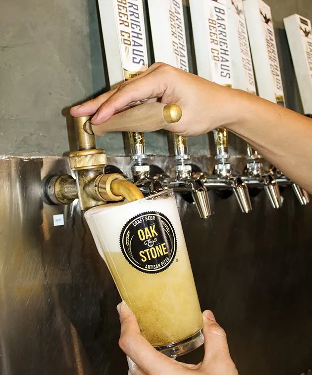 Hands pouring frothy beer from a brass tap into a branded glass.