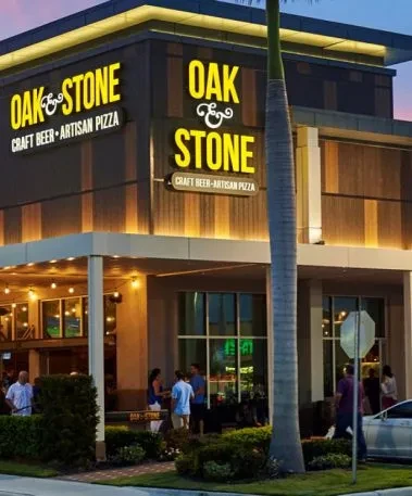 Modern OAK & STONE restaurant facade, illuminated at dusk, with people.