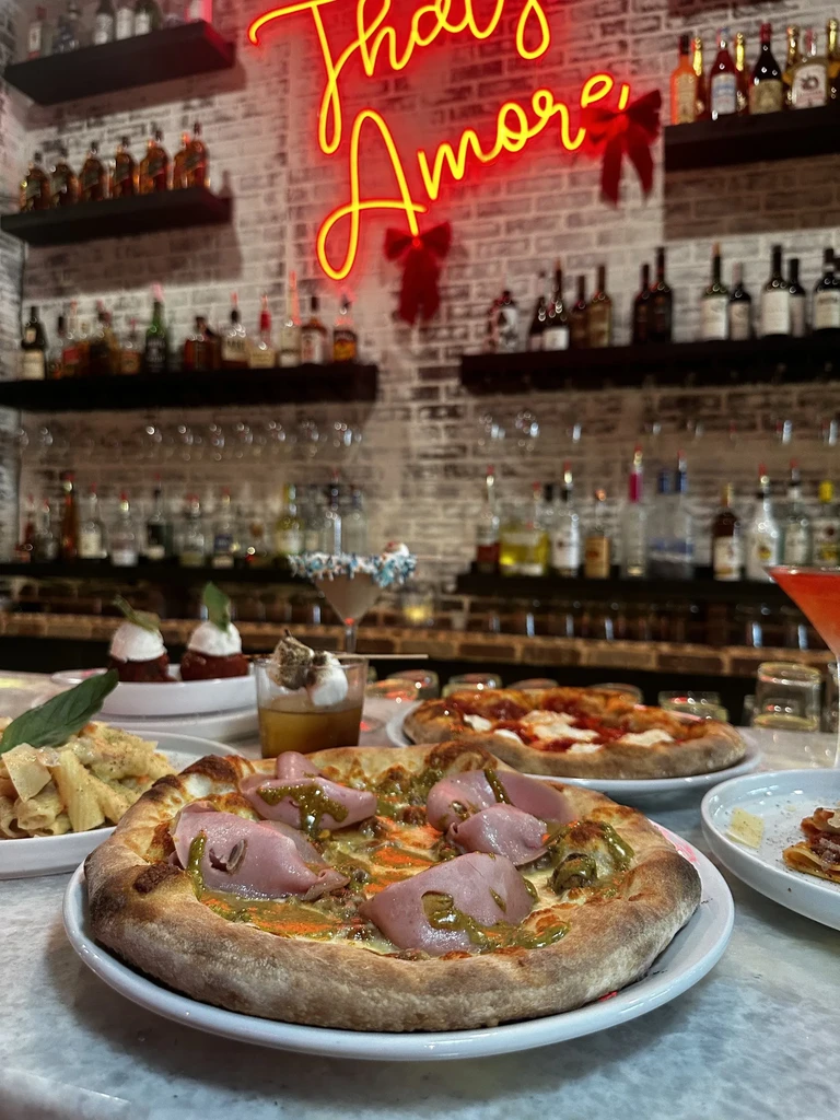 Italian food and cocktails on a bar, with a 'That's Amore' neon sign.