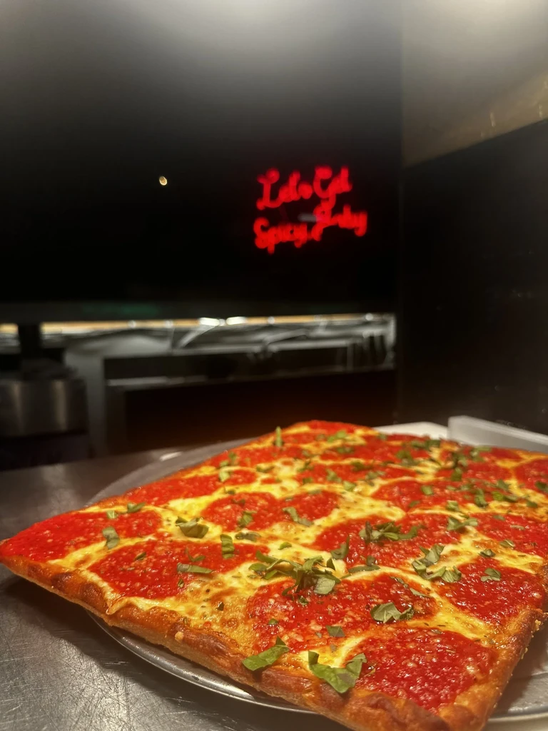 Square-cut pizza with thick crust, tomato, melted cheese, and fresh basil.
