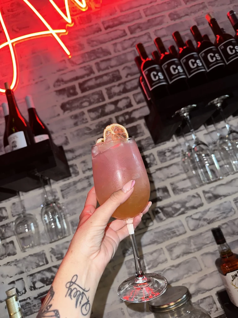 Hand with tattoo holding a gradient cocktail in a lively bar.