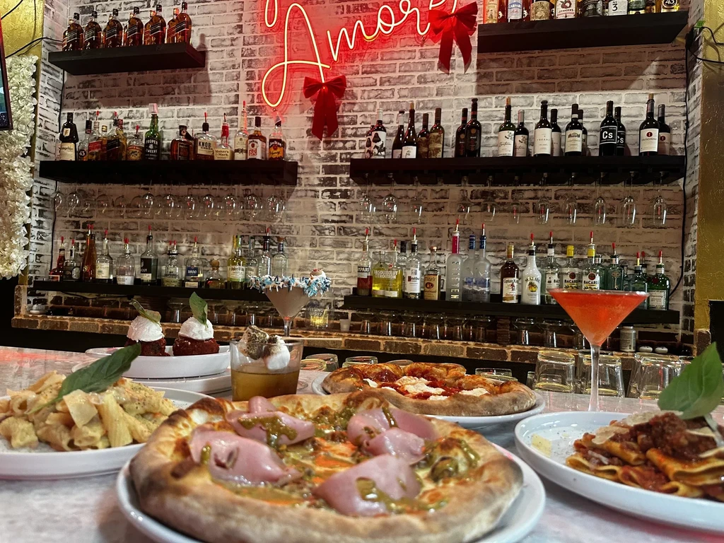 Italian pizzas, pasta, cocktails, and an 'Amore' neon sign at a bar.