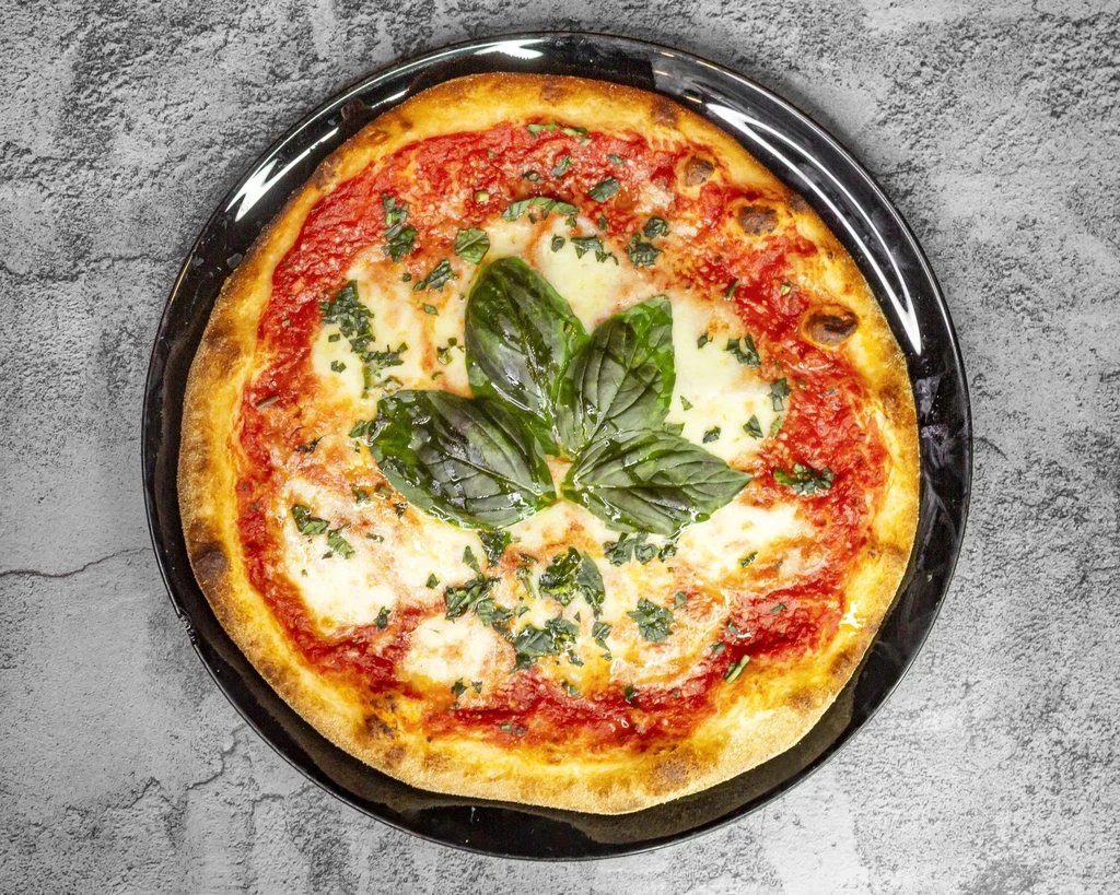 Classic Margherita pizza with fresh basil on a round black plate.