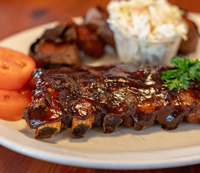 Barbecued ribs with glistening sauce, red tomato slices, and coleslaw.