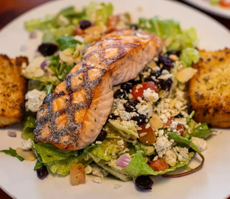 Grilled salmon salad with cheese, dried fruit, and garlic bread.