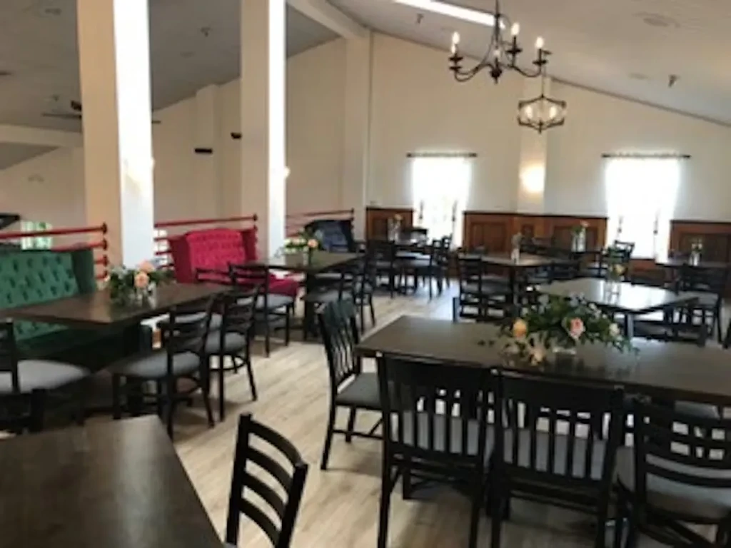 Bright, empty dining room with set tables, floral centerpieces, and chandeliers.
