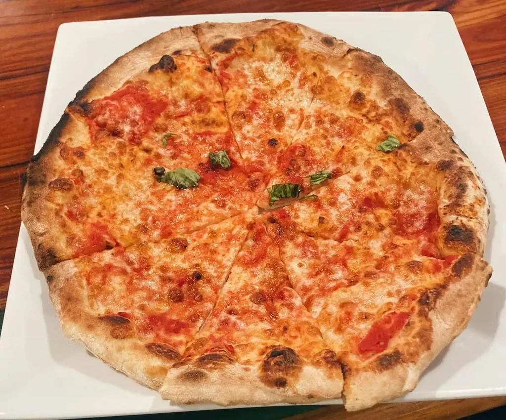 Close-up, top-down of sliced Margherita pizza with basil on a plate.