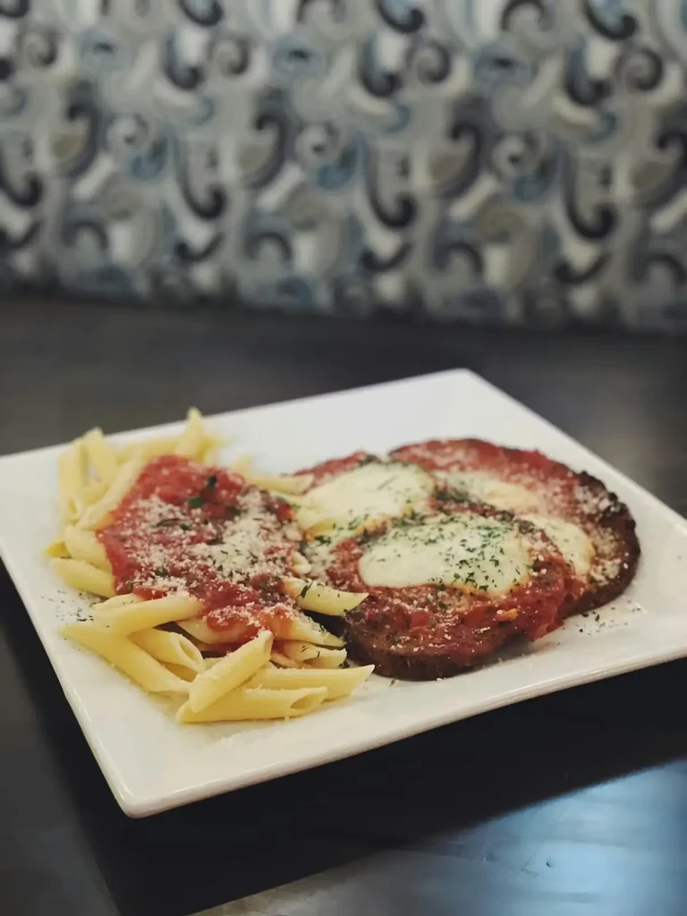 Penne pasta, breaded cutlets with marinara and cheese on a plate.