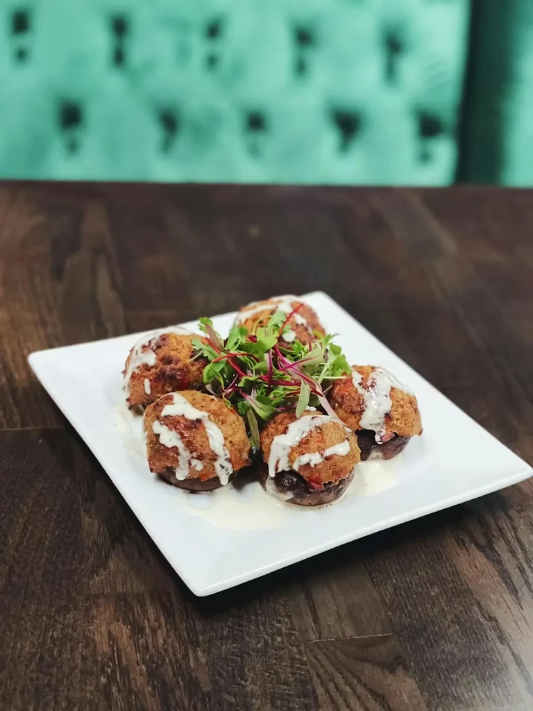 Five stuffed mushrooms with creamy white sauce and microgreens on a white plate.